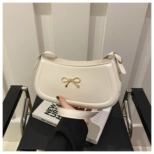 Detailed close-up of cream shoulder bag featuring a gold metal bow clasp and sleek faux leather