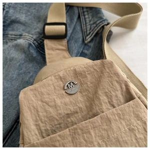 Detail of waterproof nylon chest bag with metallic M FASHION logo and textured fabric