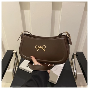 Detail of a dark chocolate shoulder bag with a gold metal bow and smooth finish