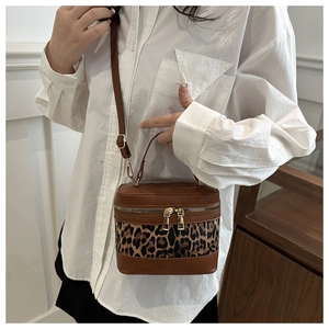 Detail of leopard print vanity bag with brown leather and gold zippers on white shirt