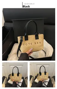 Detail of a beige woven tote bag featuring black leather handles and TOTE BAG embroidery