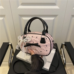 Pink pleated crossbody bag with black bow accents and pearl lace charm detail