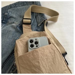 Macro detail of beige nylon chest bag showing texture and front pocket for smartphone