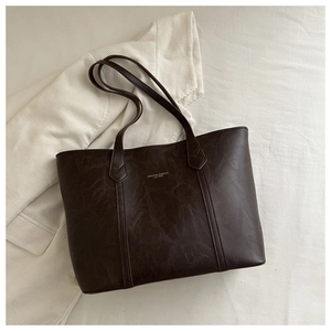 Detail of deep brown tote bag with leather texture and gold lettering on white bedding
