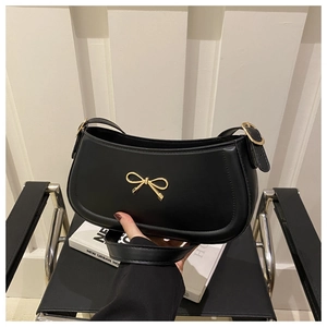 Detail of black matte leather shoulder bag featuring a gold metal bow and buckle strap
