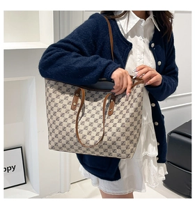 Detailed view of large tote bag with gray letter print and brown leather handles on shoulder