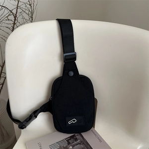 Minimalist black canvas crossbody bag with adjustable strap on a white chair background