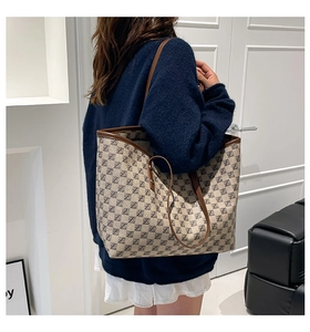 Detail of a large retro tote bag with monogram print and brown leather straps on a model