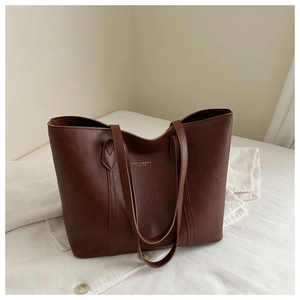 Detailed shot of brown leather tote bag with gold lettering on soft corduroy shirt