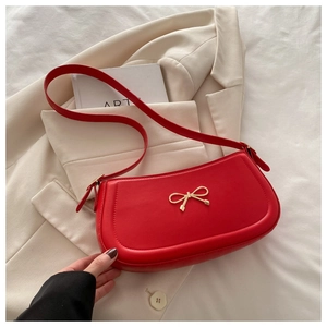 Detail of red underarm bag featuring a metallic gold bow accessory and fine leather stitching