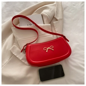 Detail view of red faux leather shoulder bag featuring a gold bow buckle on smooth PU