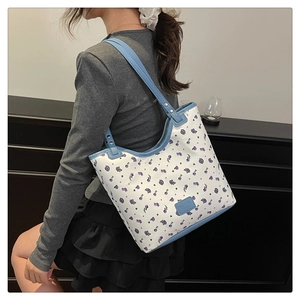 Vue détaillée du sac cabas en toile à fleurs avec anses bleu clair porté à l'épaule