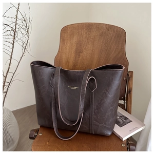 Detailed texture of dark brown leather tote bag with gold lettering on a wooden chair