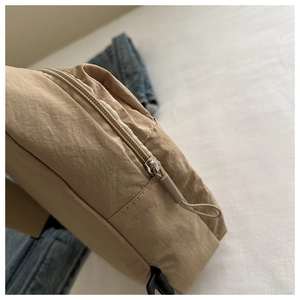 Close-up of rope zipper pull and wrinkled nylon texture on a khaki crossbody bag