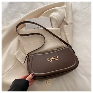 Detail of dark brown leather underarm bag featuring a gold bow buckle and smooth texture