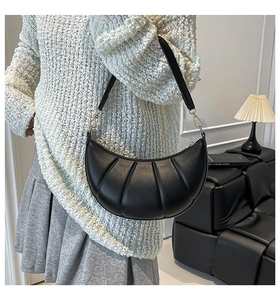 Detail shot of black crescent shoulder bag with pleated texture and gold hardware links