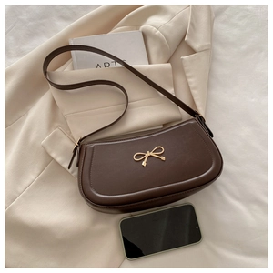 Detail of brown leather crescent bag featuring a golden bow accent on a beige blazer
