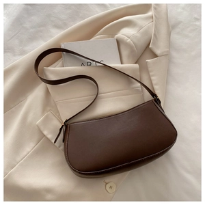 Detail view of a dark brown crescent baguette bag on a beige blazer background
