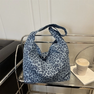Blue leopard print canvas hobo tote bag with wide shoulder strap on a display shelf