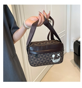 Detail of crossbody bag featuring geometric brown patterns and a white graffiti smiley face