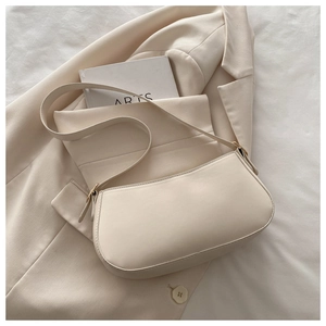 Close-up of minimalist beige baguette bag with gold buckle on a cream blazer