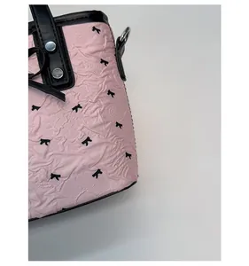 Detail of pink bow-patterned pleated fabric with black leather handle and metal rivets