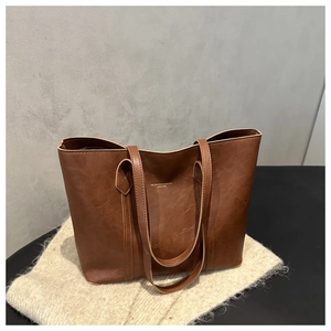 Close-up of brown textured leather tote bag with gold stamped lettering and slim straps