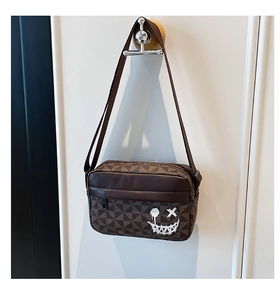 Detail of crossbody bag with brown geometric pattern and white graffiti smiley face