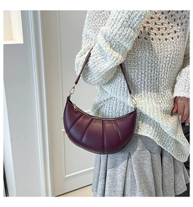 Detail of burgundy crescent shoulder bag with pleated leather texture and gold zipper