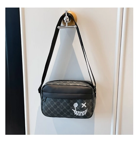 Detail shot of a dark grey patterned crossbody bag with a white graffiti smiley face icon