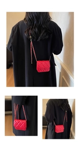 Detail of red quilted mini crossbody bag with golden chain strap on a black coat