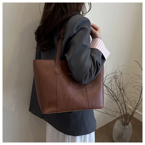 Brown faux leather tote bag on shoulder of model in grey suit for office look