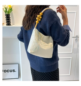 Detail of embroidered leaves on a beige fabric shoulder bag with wooden beaded strap