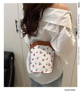 Detailed view of bucket bag featuring cherry patterns and brown leather strap detail