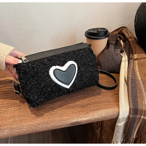 Détail du sac en laine d'agneau noire avec écusson en cœur et fermeture éclair dorée