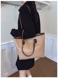 Detalle de un bolso tote grande caqui con asas marrones oscuras llevado por una modelo