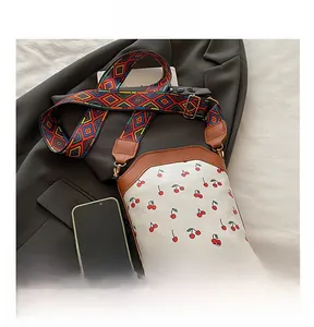 Close-up of cherry print crossbody bag with brown leather trim and ethnic style wide strap