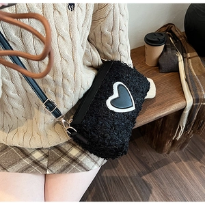 Détail du sac bandoulière en peluche avec écusson cœur noir et bandoulière en cuir souple