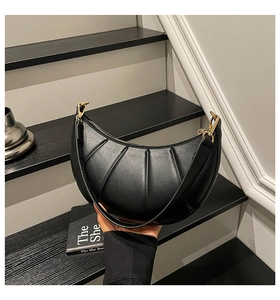 Detail of black crescent moon bag with pleated texture and gold hardware on stairs