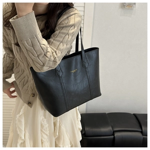 Detail of black textured leather tote bag featuring golden lettering and dual straps