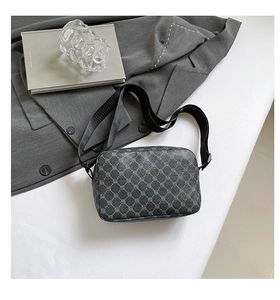 Close-up of small crossbody bag with geometric pattern on gray suit and book