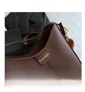 Détail du sac seau en cuir marron avec logo fashion et breloque pompon en peluche