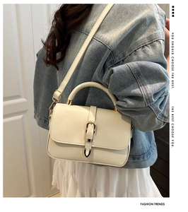 Detail of a creamy white small square bag with a golden buckle and leather handle