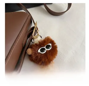 Détail d'un pendentif animal en peluche marron avec lunettes noires sur un sac en cuir