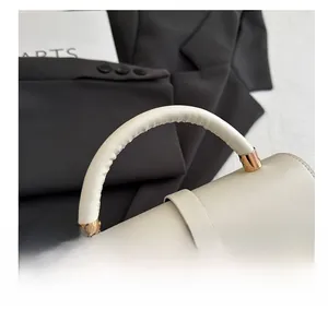 Close-up of a creamy white PU leather handbag featuring a padded handle and gold metal clasp