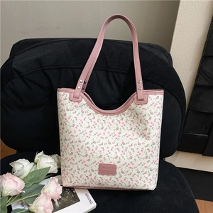 Sac cabas en toile à imprimé floral avec anses en cuir rose posé sur une chaise noire
