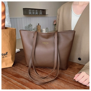 Primer plano del bolso tote marrón oscuro con letras doradas sobre cuero mate premium