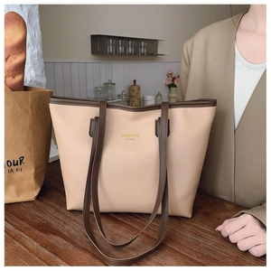 Detalle de un bolso tote grande beige con asas marrones sobre una mesa de madera