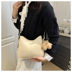 Détail du sac seau crème avec logo doré et pendentif d'ours en peluche marron