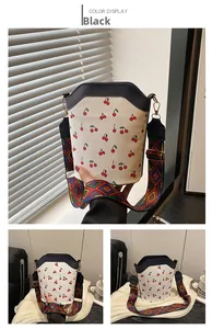 Detail of white bucket bag with cherry print, black trim, and geometric patterned strap